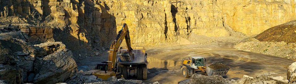 Bagger und Radlader beim Beladen eines Muldenkippers im sonnenbeschienenen Kalksteinbruch